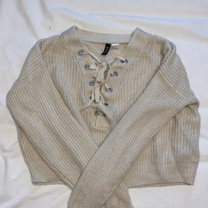 Stickad tröja - Stickad tröja med snörning där fram. Färgen är beige/kräm vit