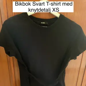 Svart T-shirt i bomull med knyt detalj som kan viras & knytas på olika sätt 