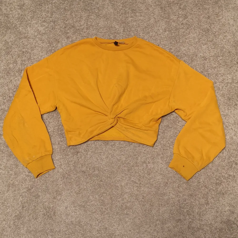 En supersnygg senapsgul tröja med knytdetalj. Croppad och i storlek XS från devided. Har en liten fläck vid ärmslutet(bild 3) och är lite nopprig men annars i bra skick. . Tröjor & Koftor.