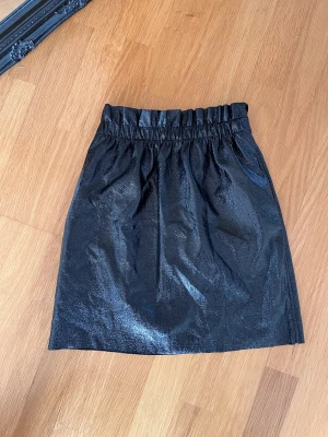 Minikjol - Kjol i svart läder imitation! Såå fin och perfekt till fest!  Svart blankt tyg som ser lite skimmrigt ut i mörker!! Mjuk och stretchig! Superskön!!!