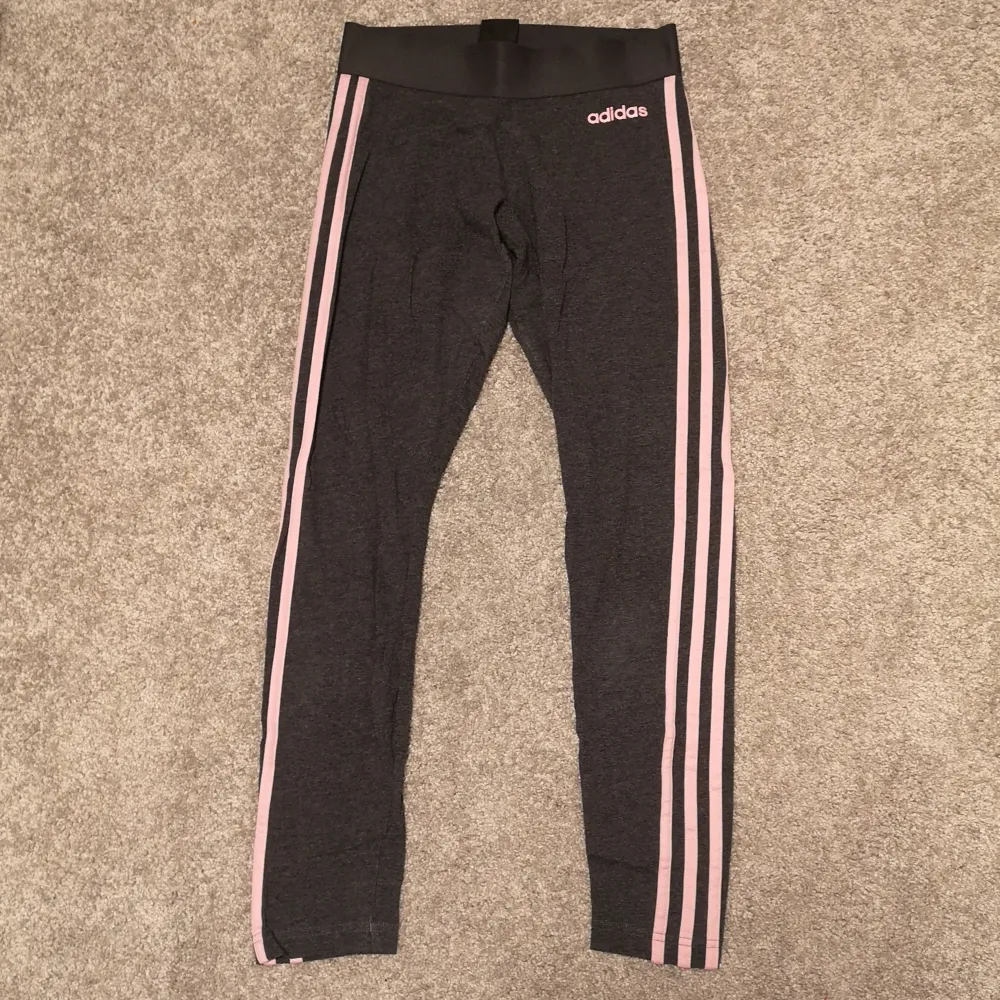 Ett par supersnygga Adidas tights i en mörkgrå färg med rosa streck. Säljer då de blivit för korta för mig. I superbra skick i storlek XS. . Jeans & Byxor.