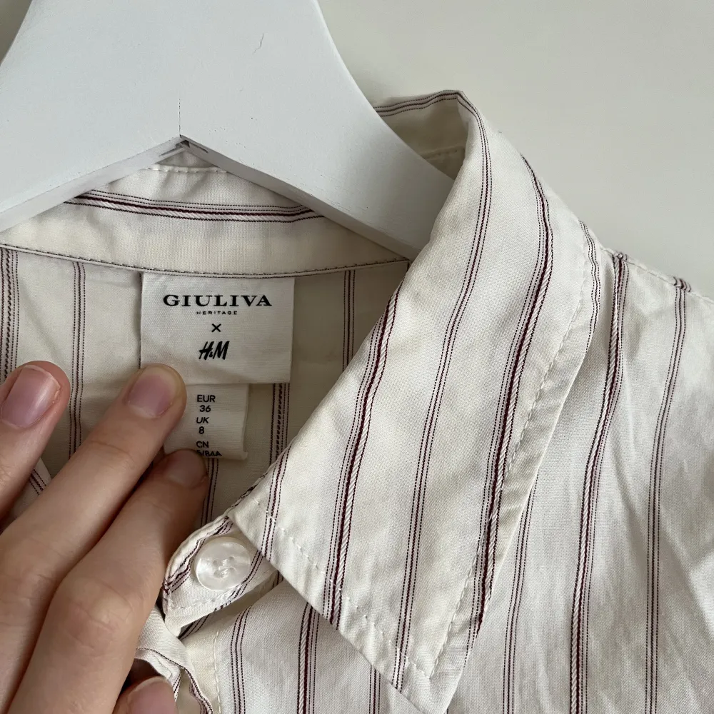 Figursydd beige skjorta med lila ränder från HM x Giuliva Heritage.  Smäcker och ger ett ”dressat” intryck, men kommer tyvärr inte till användning hos mig. Passar xs-s. Är tyvärr inte struken vid försäljning. . Skjortor.