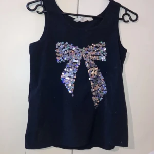 Svart festtopp  - Säljer detta snygga linnet med mig paljetter format som en rosett på, från h&m, då den ej kmr till användning. Använd fåtal ggr och är i bra skick! 🎀
