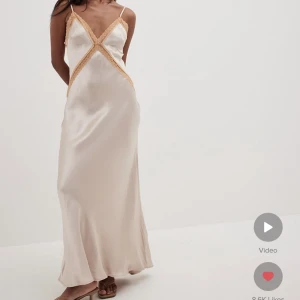 Lång klänning i satin  - Lång klänning i satin går några cm över fötterna på mig som är 171cm. Klänningen är beige/champagne färgad med orangea spets detaljer. Nypris 799kr