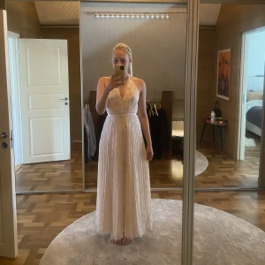 Balklänning - En oanvänd balklänning som fortfarande har prislappen kvar. Klänningen är champangefärgad med fina detaljer i glitter. Jag är 173 cm lång. Nypris 1300