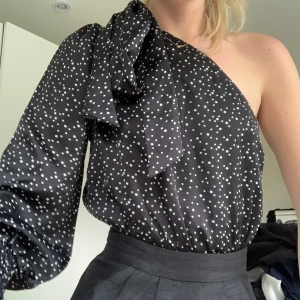 Prickig oneshoulder body - Prickig oneshoulder body från Saint Genies i storlek S. Siden liknande tyg. Jättefint skick! Band på ena axeln som går att knyta i rosett som på bilderna. Dragkedja på ena sidan för att knäppa