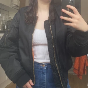 Svart Bomberjacka - Svart super klassisk bomberjacka med orange innerfoder. Använd men i gott skick. Säljer pga för liten för mig. 