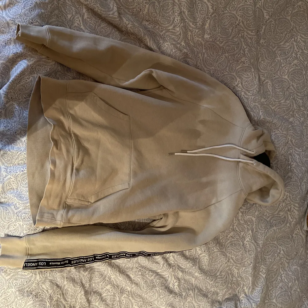 En beige hoodie från H&M i helt nytt skick. Använt väldigt sällan. Hoodien har tryck längs armarna men inget på ryggen. Riktigt clean, perfekt för sommaren! Skick 9/10. Tröjor & Koftor.
