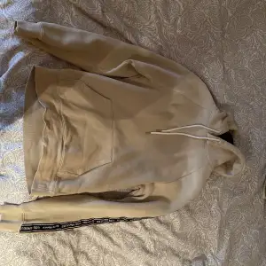 En beige hoodie från H&M i helt nytt skick. Använt väldigt sällan. Hoodien har tryck längs armarna men inget på ryggen. Riktigt clean, perfekt för sommaren! Skick 9/10