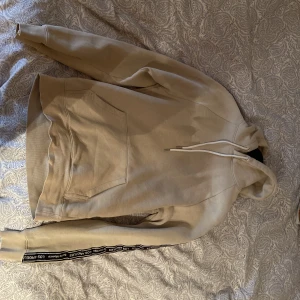 Beige Hoodie från H&M - En beige hoodie från H&M i helt nytt skick. Använt väldigt sällan. Hoodien har tryck längs armarna men inget på ryggen. Riktigt clean, perfekt för sommaren! Skick 9/10