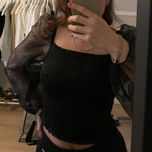 Svart mesh-topp - Från NAKD. Smockad topp med organza-armar. Fin kvalitet, stretchig