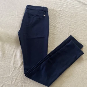 Tommy Hilfiger kostymbyxor  - Marinblå kostymbyxor från Tommy Hilfiger. Strl 2. Slim fit.  (Har en liten noppra på baksidan av ena benet, inget tydligt märkbart men syns på nära håll. Se bild 3)