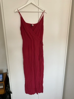 Maxiklänning - Supersnygg maxiklänning i hallonrött. Omlott överdel med knytning i midjan. Hög slits. Jättefin på! Passar definitivt INTE en vanlig storlek 42 skulle säga att den sitter mer som en 38 speciellt kring bysten. Hel och ren.