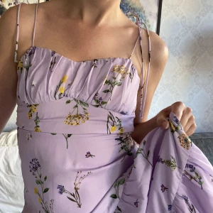 Lila sommarklänning xs - En vacker sommarklänning med blomster. Dragkedja i ryggen och knyts i axelbanden. Slutar strax nedanför knät 