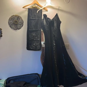 Klänning  - Svart klänning i väldigt skön silkesliknande material. Har svarta blommor vid ena sidan av urringninen. Finns även en extra sjal i samma material. Priset kan diskuteras.