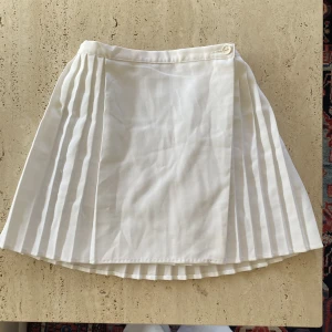 Kjol - Vit veckad kjol som korsars över med knapp. 