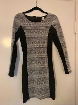 Svart klänning med mönster - Svart långärmad klänning med vita mönster. Liten dragkdja på ryggen. Bara använd nån gång. 