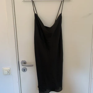Satin klänning  - En svart satin klänning, den går korsat där bak och lite pösig på framsidan, går halvvägs till knäna på mig som är 170+cm💕