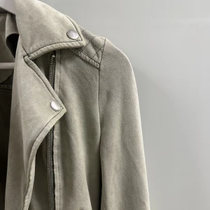 Jacka  - Jacka i mockaimitation, ljusgrön färg med bälte. Ej avtagbart. 