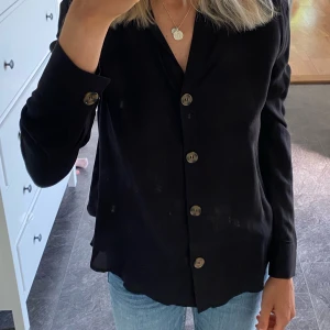Blus med knappar  - Svart blus med bruna knappar. Tunt skönt material. Väldigt fint skick då den knappt är använd. 