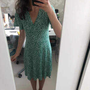 Klänning - Säljer en grön/vit blommig medellång klänning från Indiska, strl. XS. Använd 1 gång, i mycket bra skick! Har sytt ihop V-ringen lite, men den går lätt att sprätta upp om man vill det😊 (tredje bilden).
