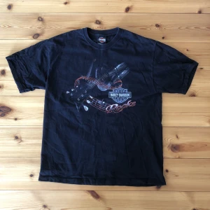 Harley davidson t-shirt - Säljer en fet vintage HD T-shirt! Fint skick förutom ett litet hål som inte märks. Storlek på tröjan är L men den är uppsydd några centimeter så den är lite kortare än orginal. Längden är 72 cm.