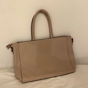 Väska  - Väskan är några år gammal. Den har några få repor men annars är den väldigt fin. Färgen är en blandning mellan rosa och beige. 