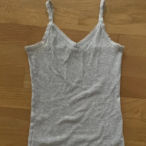 Basic linne 🤍 - Grått ribbat linne med spetsdetaljer 🤍Köpt på H&M, vet inte storlek pga lappen borttagen, men tror det är en 158/164 - passar mig som har storlek XS  (obs lite missfärgning på insidan vid armhålan, se sista bilden😊) kontakta för fler bilder
