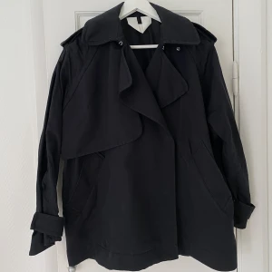 Kort trenchcoat  - Fin kort svart trenchcoat från Arket! Fin kvalitet och passform, perfekt nu till hösten. Använd fåtal gånger så fint skick! 