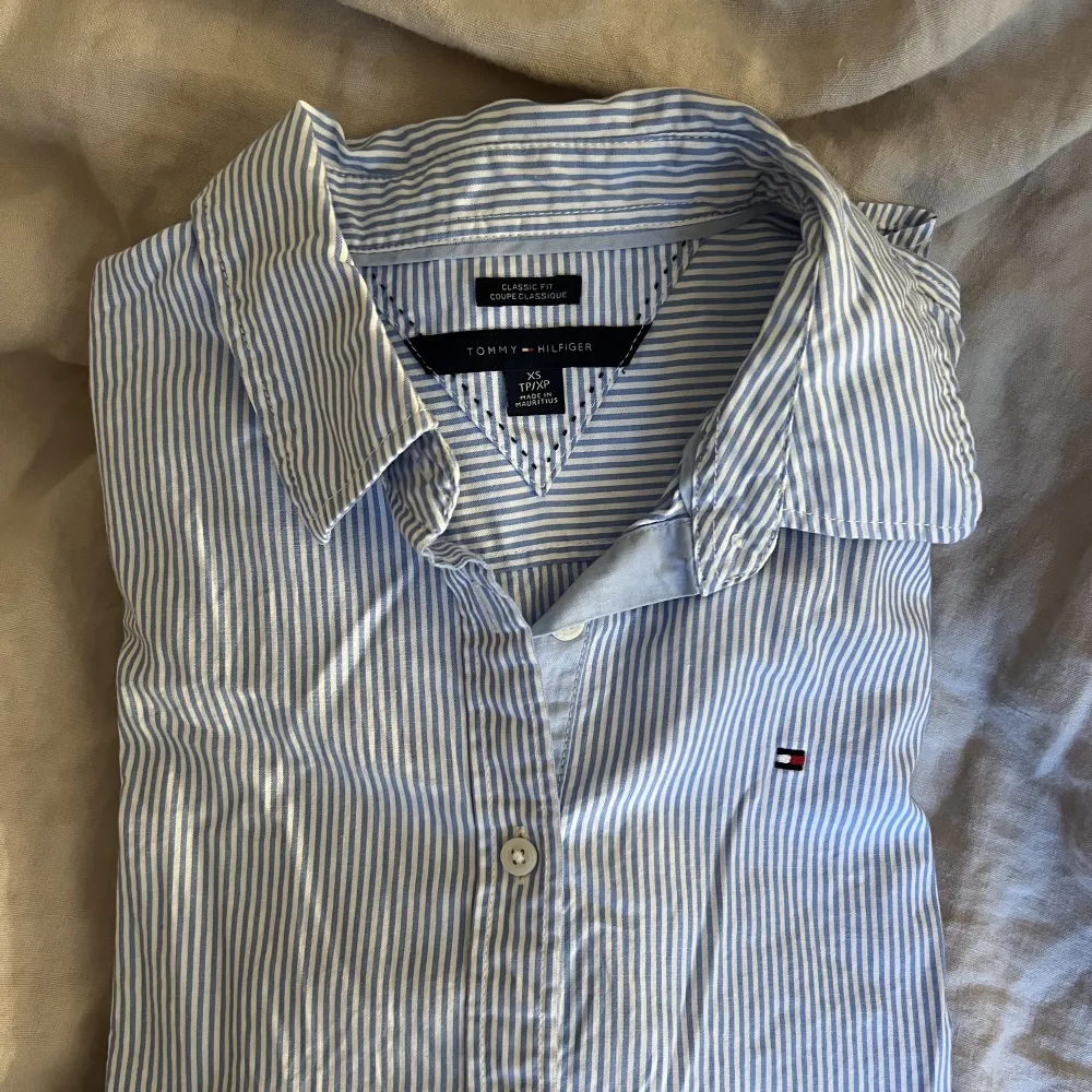 Randig skjorta från Tommy Hilfiger i ljusblå och vit. Storlek XS som ger en figursydd passform. Använd fåtal gånger, i mycket gott skick.🩵. Skjortor.