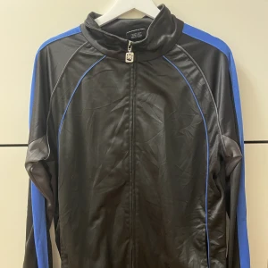 Svart träningsjacka - Sjukt fin träningjacka med blåa detaljer. Köpt secondhand. Jättebra skick. 