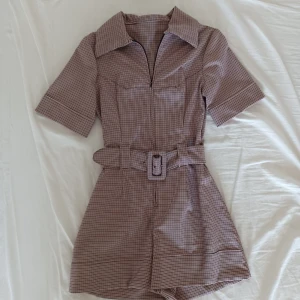 Handsydd playsuit - Handsydd playsuit med bälte. Finrutigt mönster i cerise, offwhite och svart. Perfekt skick