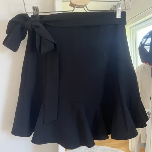 svart minikjol med volang och knytning - svart kjol med volang nedtill, knytning runt midjan och dragsko💓sparsamt använd utan defekter!