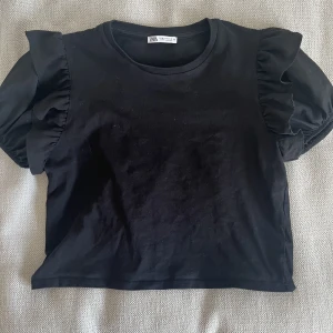 topp med puffärmar och volanger - svart topp från zara med volanger och puffärmar. knappt använd, ser ut som ny. skulle säga att den är lite liten i storleken. skriv för frågor. köparen står för frakten.