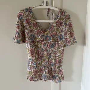 Färgglad blommig blus  - Färgglad blus som har rosa och blåa blommor med gröna löv på. 