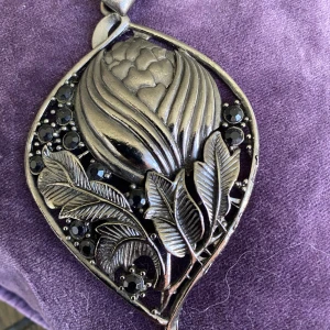 Halsband art deco - Ett vackert halsband med stort hänge i art deco stil dekorerat med svarta stenar och blomster   Okänt material 