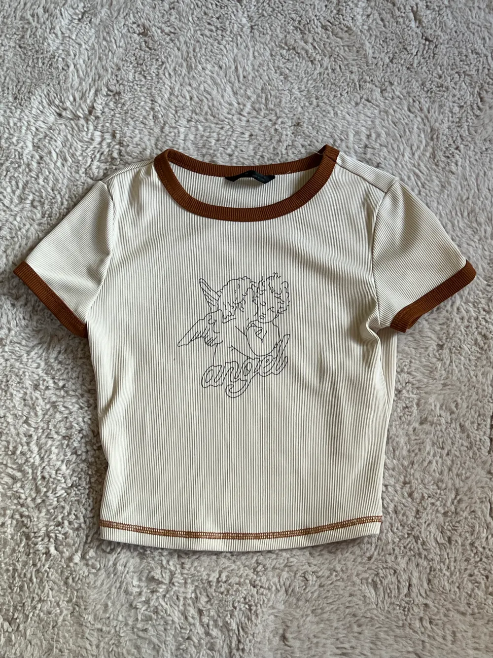 Beige T-shirt med bruna detaljer och två änglar på framsidan samt texten Angel. T-shirts.
