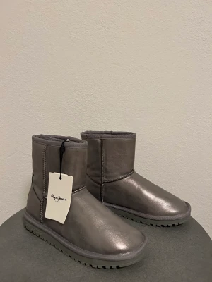 Silver ugs från Pepe Jeans London  - Säljer min dotters silver (metallic) uggs liknande boots från Pepe Jeans London. Skorna är helt oanvända och väldigt snygga. 