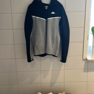 Nike tech fleece - Säljer nu min grå/svarta Nike Tech Fleece för ett bra pris på 700, ny pris på denna hoodie är ca 1350kr. Den är knappt använd har bara använt den max 10 gånger. Jag står för frakten!!