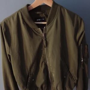 Grön jacka - Har använts några gånger. Jag tror att den köptes på second hand. Finns några pyttesmå trådar runt kedjan på armen och luktar pyttelite men inte så att man märker det om inte man sätter näsan på den. Annars i bra skick. Är inte vattentät.