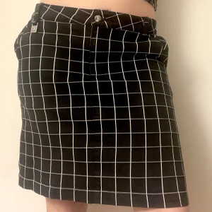 Svart vitrutig midikjol - Kjol i svart med vitt rutmönster. Går typ till över knäna på mig som är 165 cm. Den står ut lite och har en slits där bak. Har även inbyggda shorts i kjolen. Lite stor på mig som brukar ha s-m men funkar lågmidjat. Kan mötas nära Mariatorget eller posta. 