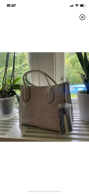 Väska - Beige väska med mycket utrymme i. Flera fack med och utan dragkedjor. Kommer med axelband oxå. Helt oanvänd med lappen kvar.  Köpt för 65 amerikanska dollar (ca 700kr) plus frakt (ca 100kr) och tull (strax över 100kr). Säljes för 200kr.