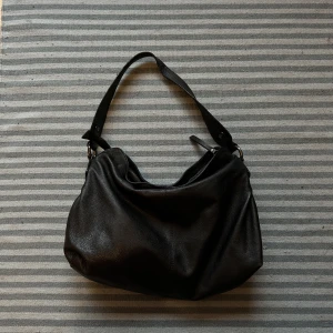 Shoulderbag skinn - Rymlig väska i äkta skinn med dragkedja. Mycket sparsamt använd och fint skick. Inga fläckar eller missfärgningar. Blommigt mönster på insidan och har innerfack. 