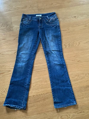 Lågmidjade raka jeans med coola fickor  - Lågmidjade jeans som är ganska raka i modellen. Detaljer på fickorna både fram och bak. Är använda men har bra kvalitet. En fin blå färg med lite ”urtvättning”.