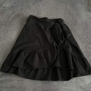 En svart kjol med volanger nedtill och omlottsknytning från Vero Moda