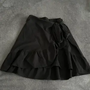 En svart kjol med volanger nedtill och omlottsknytning från Vero Moda