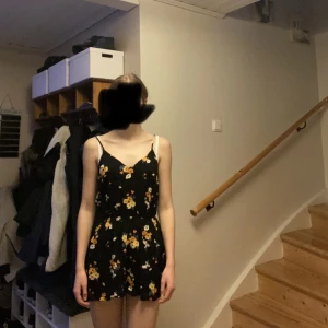 Svart byxdress  - En svart byxdress med vita, gula & oranga blommor från h&m divided☺️Den har fickor, justerbara axelband och är vringad. Använd ca 2 gånger och är felfri. Strl. 36 men känns mer som 34 för att den är så pass kort!!