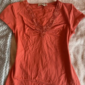 T-shirt med fina detaljer - Jättefin v-ringad t-shirt med fina detaljer vid nacken. Säljer för att den tyvärr är lite stor på mig. Ser orange ut på bilden men skulle säga att den är mer ljusröd. Skriv gärna vid frågor! (pris kan diskuteras)🫶