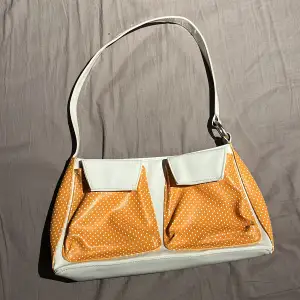 En vit & orange handväska gjord i fake skin och lack, väskan är använd och har slitningar lite runt om men inget större elelr märkbart, 