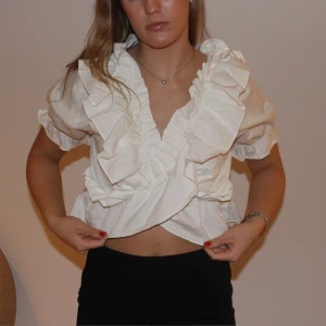 Blowy top - Beställningar görs på vår hemsida: thrifteddesign.one.    En kort vit volang top med korta ärmar. Volangtoppen har sin orginalprislapp kvar. 